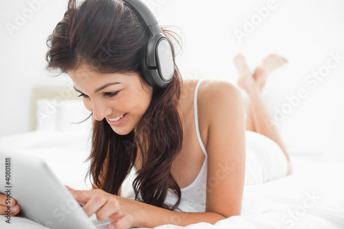 Foto: Woman with her legs crossed on the bed listening to headphones, Woman with her legs crossed on the bed listening to headphones,