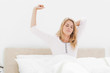 Woman upright in bed stretching with arm raised and eyes closed