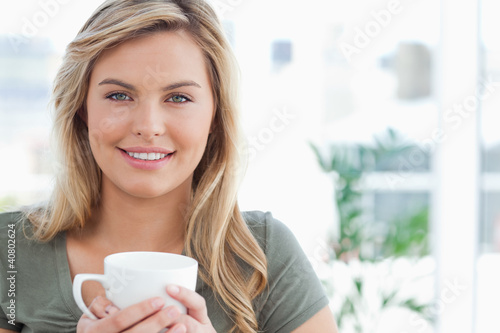 Foto: Woman holding a mug in her hands and smiling, while looking forw Woman holding a mug in her hands and smiling, while looking forw