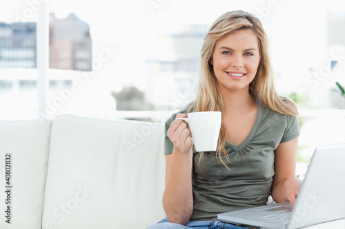 Foto: Woman looking forward and smiling as she uses her laptop and hol Woman looking forward and smiling as she uses her laptop and hol
