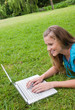 Smiling young woman lying in a park while working on her laptop