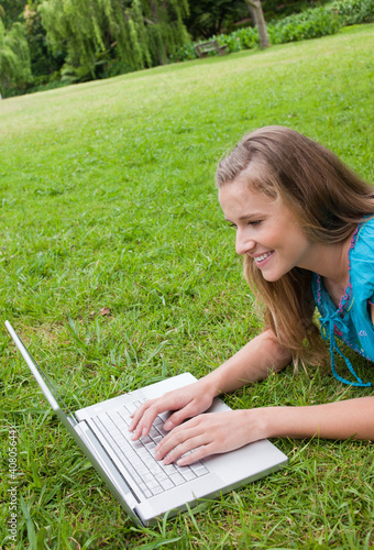 Photo: Smiling young woman lying in a park while working on her laptop Smiling young woman lying in a park while working on her laptop