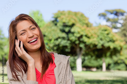Foto: Young woman laughing happily on the phone in a bright park area Young woman laughing happily on the phone in a bright park area