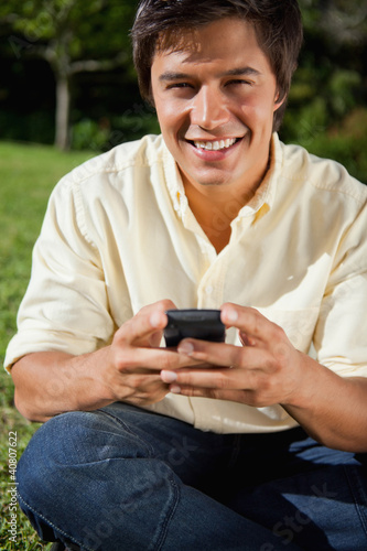 Foto: Man smiling while writing a text message as he is sitting down Man smiling while writing a text message as he is sitting down