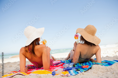 Foto: Back view of beautiful women sunbathing while sipping cocktails Back view of beautiful women sunbathing while sipping cocktails
