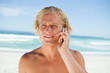 Blonde man talking on his mobile phone while standing on the bea