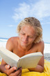 Serious man lying on his beach towel while reading a book