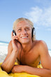 Smiling man lying on the beach while listening to music