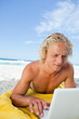 Blonde man lying on the beach while using his laptop in a very c