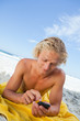 Young blonde man sending a text with his cellphone while sunbath