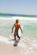 Young blonde man holding his surfboard while walking in the wate