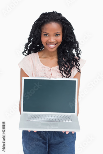Photo: A young woman is holding a laptop out in front of her A young woman is holding a laptop out in front of her
