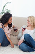 Photo: Two women are sitting on the ground leaning against a couch Two women are sitting on the ground leaning against a couch