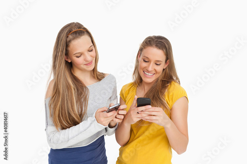 Photo: Two young women texting on their cellphones Two young women texting on their cellphones