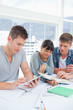 A group of students sit together using a tablet and a book to st
