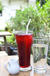 Iced roselle juice with its syrup in a small jug and drinking wa