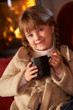 Young Girl Relaxing With Hot Drink By Cosy Log Fire