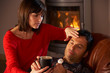 Wife Nursing Sick Husband With Cold Resting On Sofa By Cosy Log