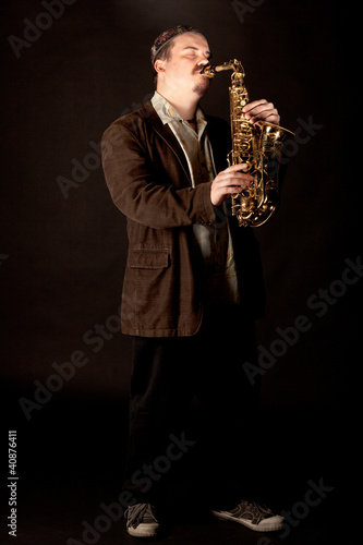 Photo: Jazzman playing saxophone with eyes closed on dark background Jazzman playing saxophone with eyes closed on dark background