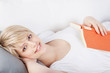 lächelnde frau mit buch auf dem sofa
