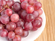 Red grape berries in white plate on straw tray closeup Red grape berries in white plate on straw tray closeup