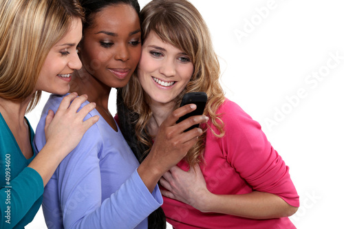 Photo: Three female friends looking at mobile telephone Three female friends looking at mobile telephone