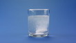 effervescent pill dropping into a glass of water over blue effervescent pill dropping into a glass of water over blue