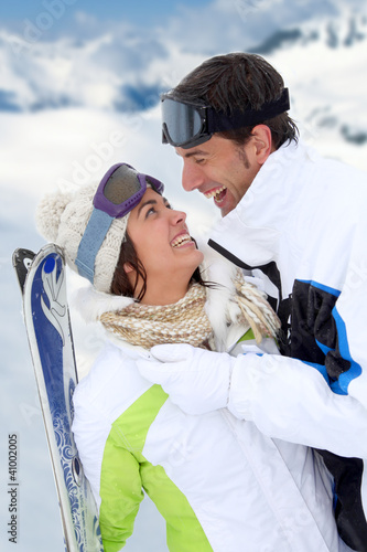 Photo: Couple standing on a snowy mountain in ski outfit Couple standing on a snowy mountain in ski outfit