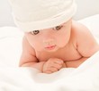 Little baby lying on the blanket and is wearing a white hat