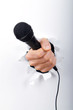 Hand holding microphone through hole in paper Hand holding microphone through hole in paper