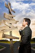 Photo: Businessman in a crossroad with confusing directional arrow sign Businessman in a crossroad with confusing directional arrow sign