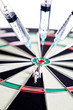 Syringes stuck in a dartboard with medical figures.