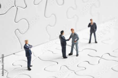Foto: Business figures shaking hands on a puzzle Business figures shaking hands on a puzzle