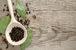 Black pepper in spoon and dry bay leaf on wooden background