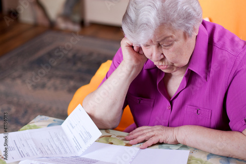Foto: Seniorin liest in Papieren und wirkt angestrengt Seniorin liest in Papieren und wirkt angestrengt