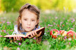 little girl lies on grass with apples and book