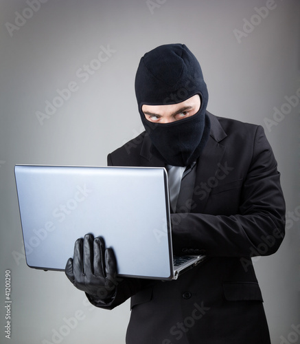 Photo: Computer Hacker in suit and tie stealing data from laptop comput Computer Hacker in suit and tie stealing data from laptop comput