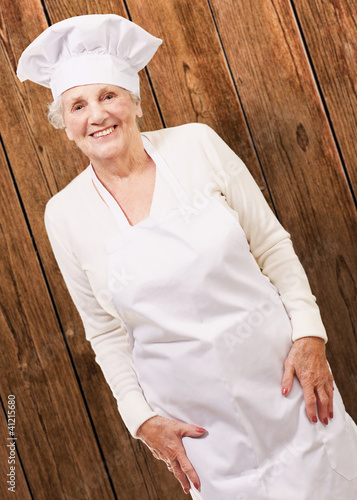 Foto: portrait of cook senior woman smiling against a wooden wall portrait of cook senior woman smiling against a wooden wall
