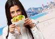 portrait of young woman holding a fresh salad against a beach