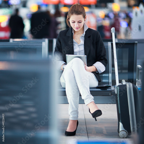 Photo: Young female passenger at the airport, using her tablet computer Young female passenger at the airport, using her tablet computer