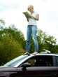Woman on top of her car in field looking at map