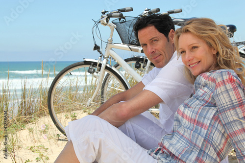 Foto: Couple with bikes sitting on the sand dunes Couple with bikes sitting on the sand dunes