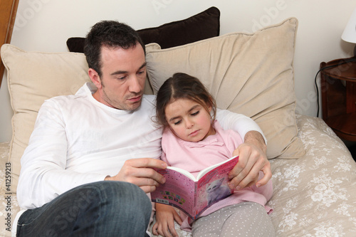 Photo: Man reading story to little girl in bed Man reading story to little girl in bed