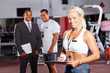 happy female gym trainer portrait with colleagues in background