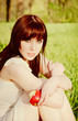 Beautiful young girl sitting on grass with apple in hand Beautiful young girl sitting on grass with apple in hand