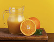 Orange juice in pitcher and oranges. Isolated on yellow Orange juice in pitcher and oranges. Isolated on yellow
