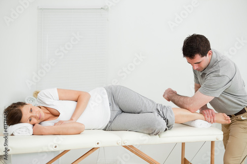 Foto: Doctor manipulating the leg of his patient while using his elbow Doctor manipulating the leg of his patient while using his elbow