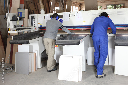 Photo: Two factory workers operating saw Two factory workers operating saw