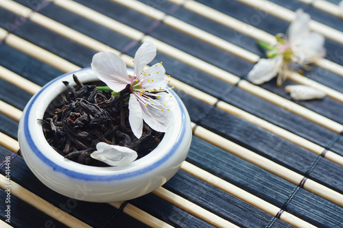 Photo: Jar of tea leaves and cherry blossoms on bamboo table Jar of tea leaves and cherry blossoms on bamboo table