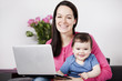 A mother using a laptop whilst holding her baby son on her lap